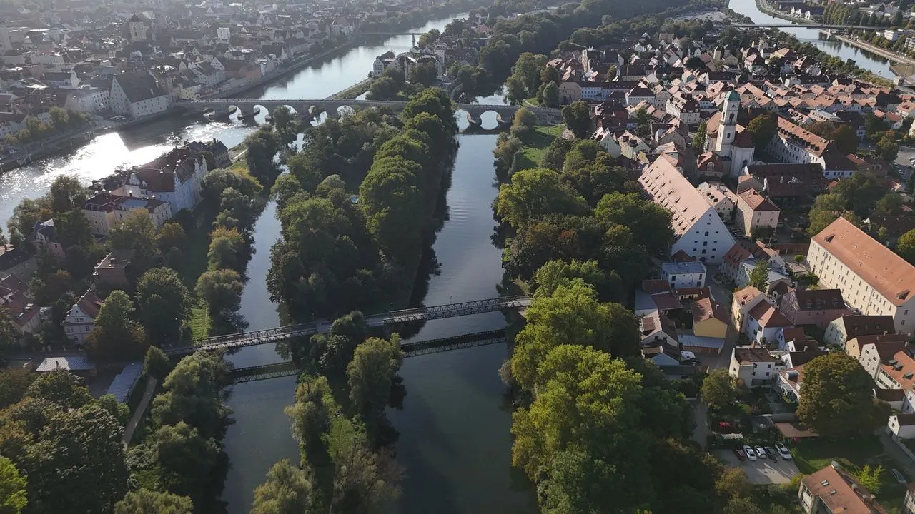 Luftaufnahme der Regensburger Donauinseln Oberer und Unterer Wöhrd: bewaldete Inseln zwischen Donauarmen, im Hintergrund die Steinerne Brücke und die Altstadt mit Stadtamhof.